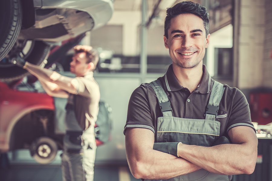 Business Insurance - Portrait of a Smiling Mechanic at a Garage With Cars and Mechanic Blurred in the Distance